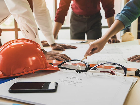 Team of professionals in a meeting, reviewing blueprints and plans with safety gear, symbolizing collaborative electrical project management