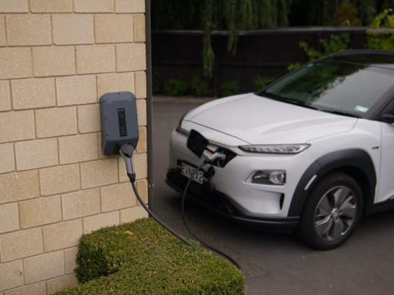 Electric vehicle charging station installed on an exterior wall, connected to a white electric car, representing sustainable electrical solutions